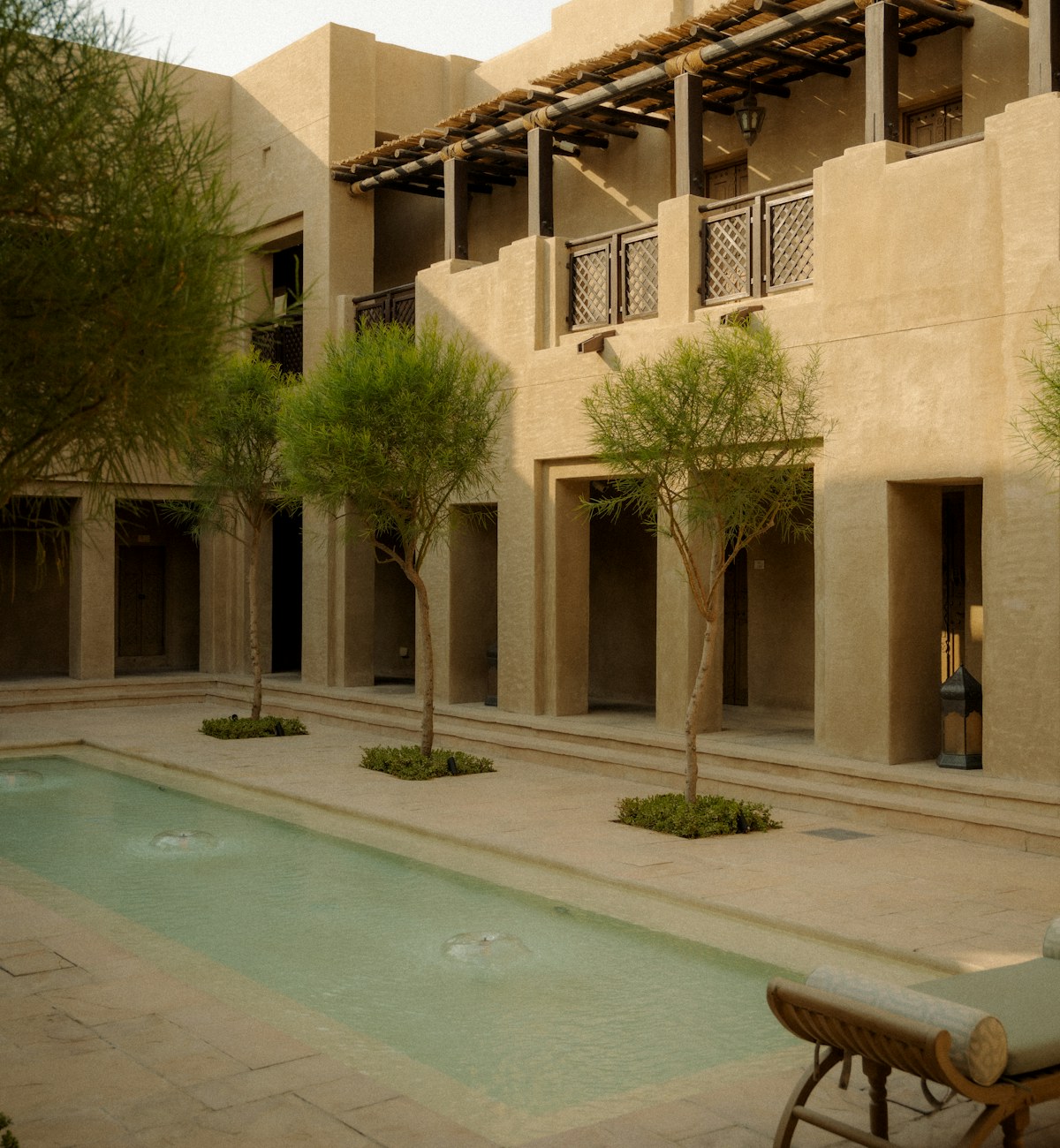 An intimate hotel courtyard with natural stone, shaded balconies and a quiet pool.