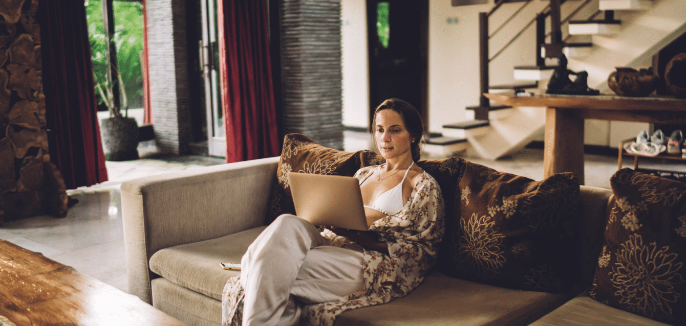 A woman relaxing on a luxury Airbnb rental’s sofa while using a laptop, representing WaveBNB’s Airbnb retargeting campaigns to convert past visitors into bookings Guest relaxing in luxury villa browsing Airbnb on laptop
