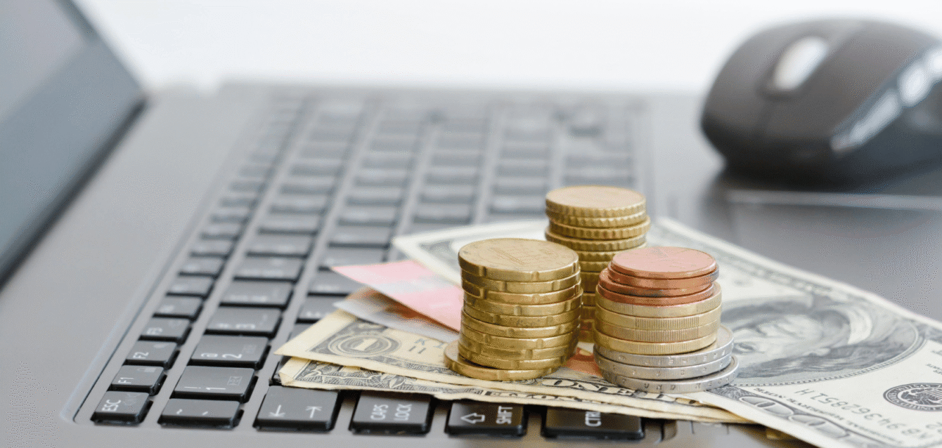 Stacks of coins and dollar bills on a laptop keyboard, symbolizing WaveBNB’s data-driven Airbnb revenue optimization and profitability strategies Coins and dollar bills on laptop keyboard representing Airbnb paid ad revenue