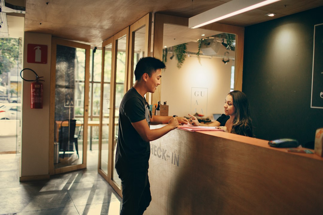 A guest and a receptionist talk across a timber check-in counter in a warmly lit lobby.